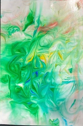 Laid on a black background is a piece of photo paper covered in green, red, blue, and yellow paint swirled together.  