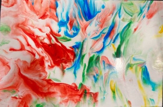 A close-up photo of colorful photo paper is on a black background. On the paper is an array of colors in a swirled pattern, the colors are red, blue, green, and yellow. 