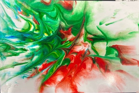 A close up of a piece of photo paper covered in an array of colors. Green, blue, yellow, and red are together. The paper is laid on a black fabric.  