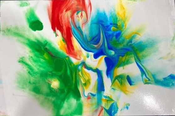 On a black background is a piece of photo paper with an assortment of colors whirled together. The colors are red, green, blue, and yellow. Green is the most prominent color included.  
