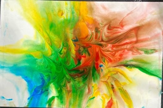 On a black background shows a close-up of colors swirled together on photo paper. The colors are orange, red, green, yellow, and blue. 