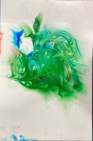 A close-up shot of a vertical piece of photo paper with abstract, swirling greens and blues. Green overpowers the other colors, with lesser amounts of blue and even smaller amounts of red. The main art doesn’t reach the edges of the paper, staying in the center. There are smudges of blue and red on the edges of the paper. It rests on a black fabric background. 