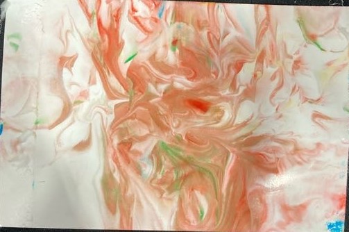 On a black background lies a white piece of paper with a large red swirl accompanied with green and blue showing.  