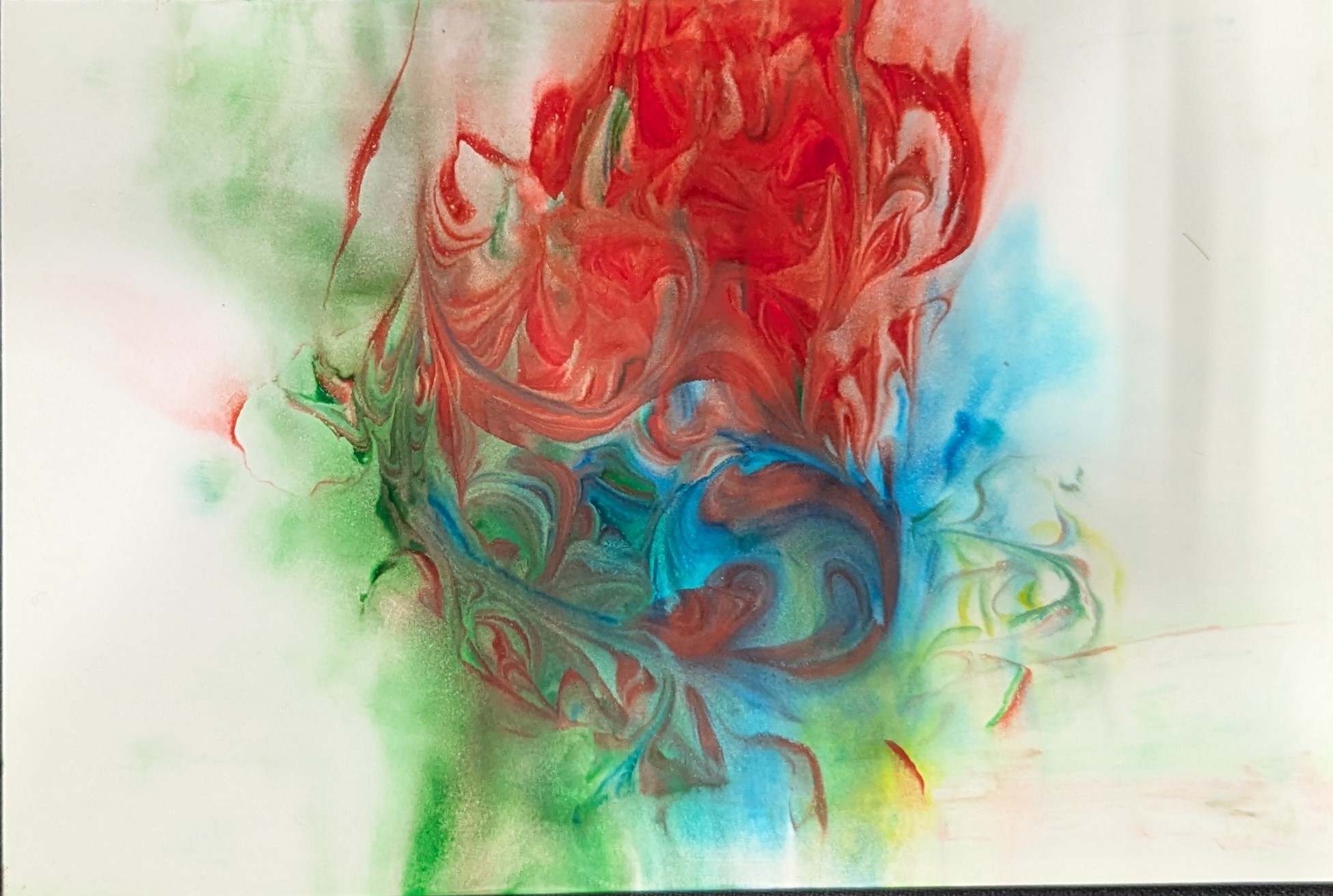 A piece of photo paper lays on a black background. The photo paper has an array of colors including red, green, blue, and yellow. They are in the center swirled together.